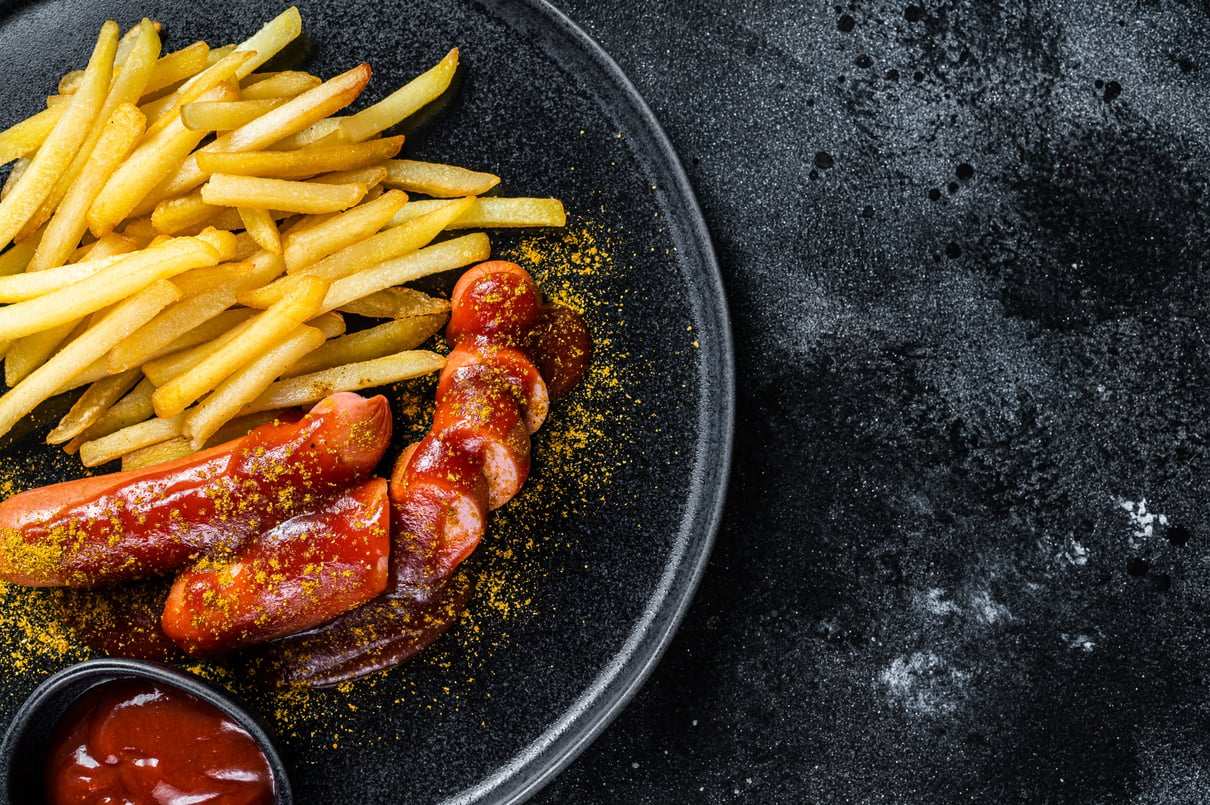 German Currywurst Sausages with French Fries on a Plate. Black Background. Top View. Copy Space